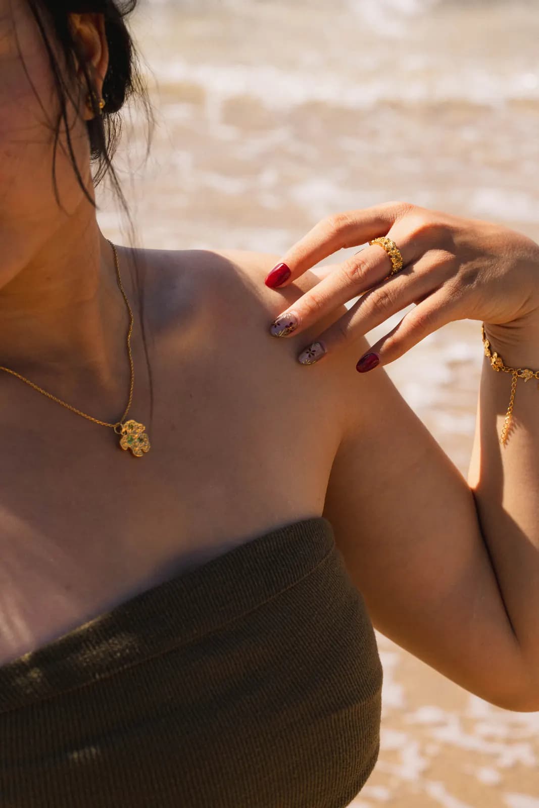Woman on a beach wearing a gold flower pendant necklace, rings and bracelet