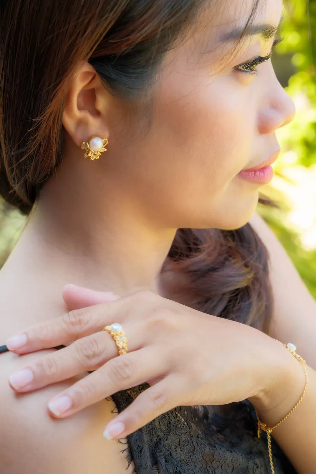 Woman in a garden wearing MEDINI pearl flower earrings, a gold ring and bracelet