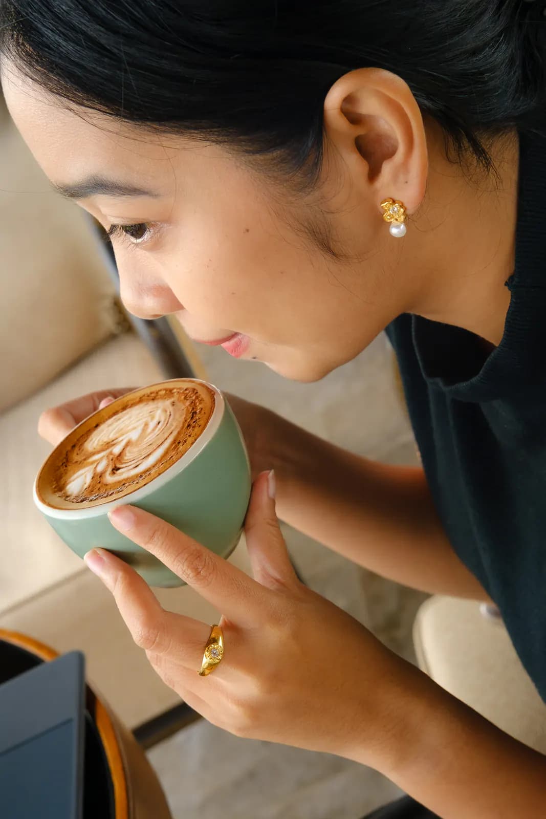 Woman with a pearl stud and gold ring holding a latte