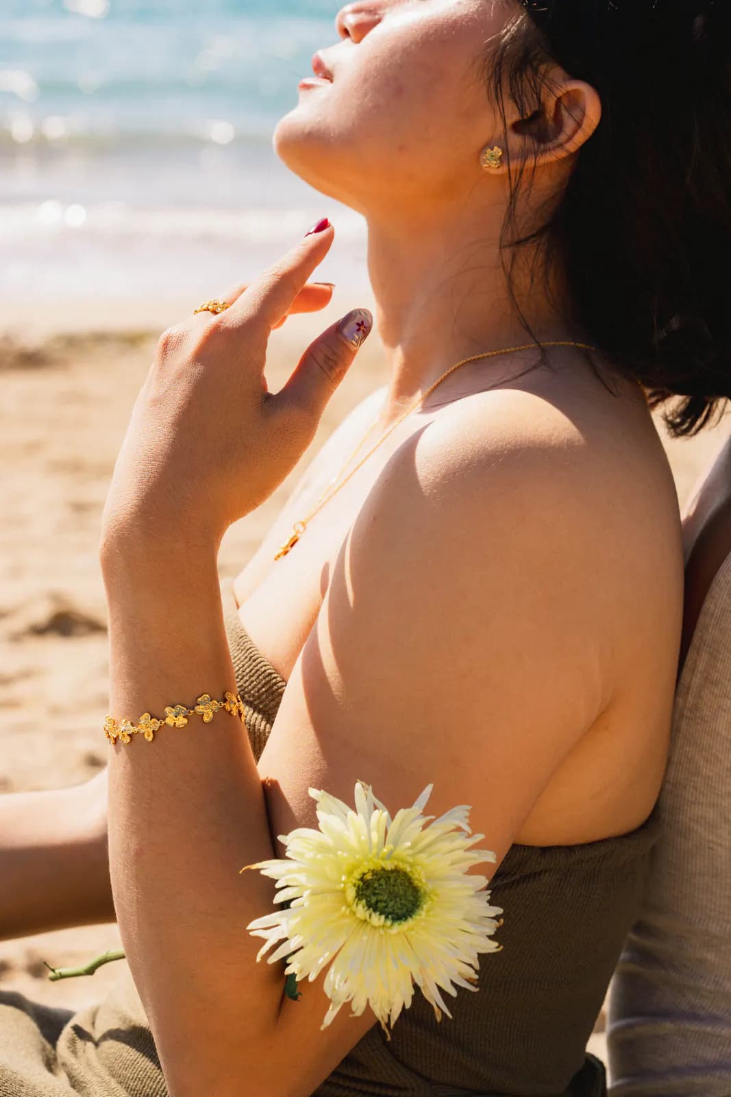 Woman tilting her face to the sun, wearing a gold floral bracelet and ring