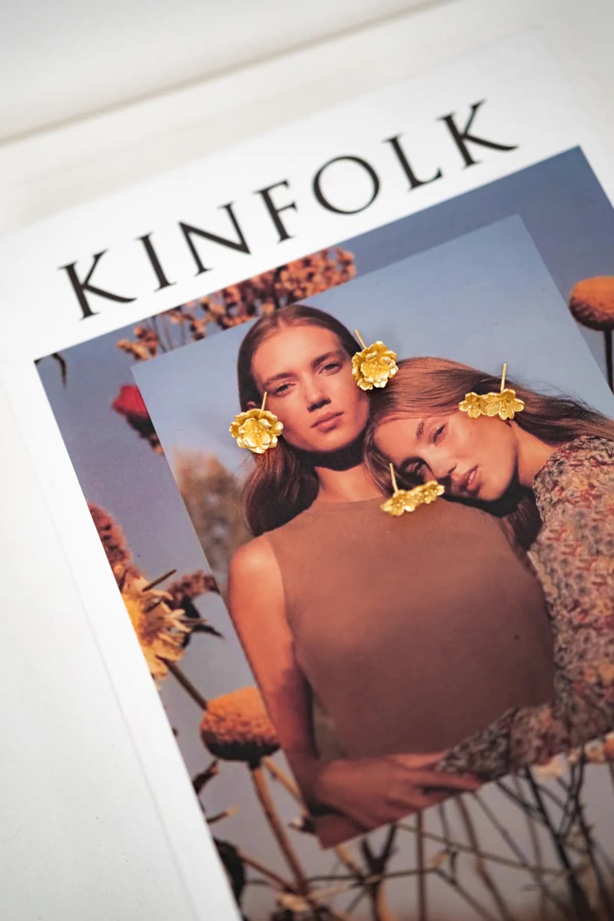 Gold flower earrings placed on a magazine cover showing two women