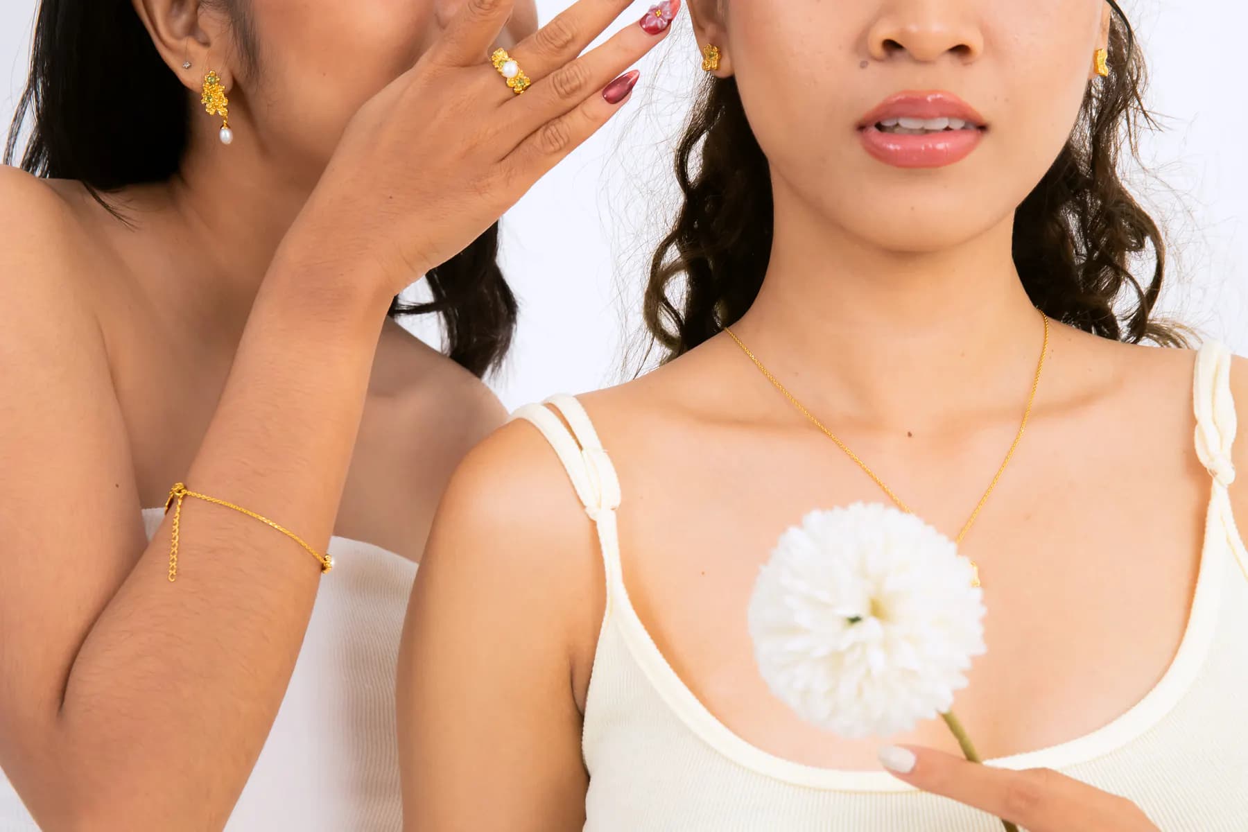 Close crop of two models with gold earrings, a flower pendant and bracelet
