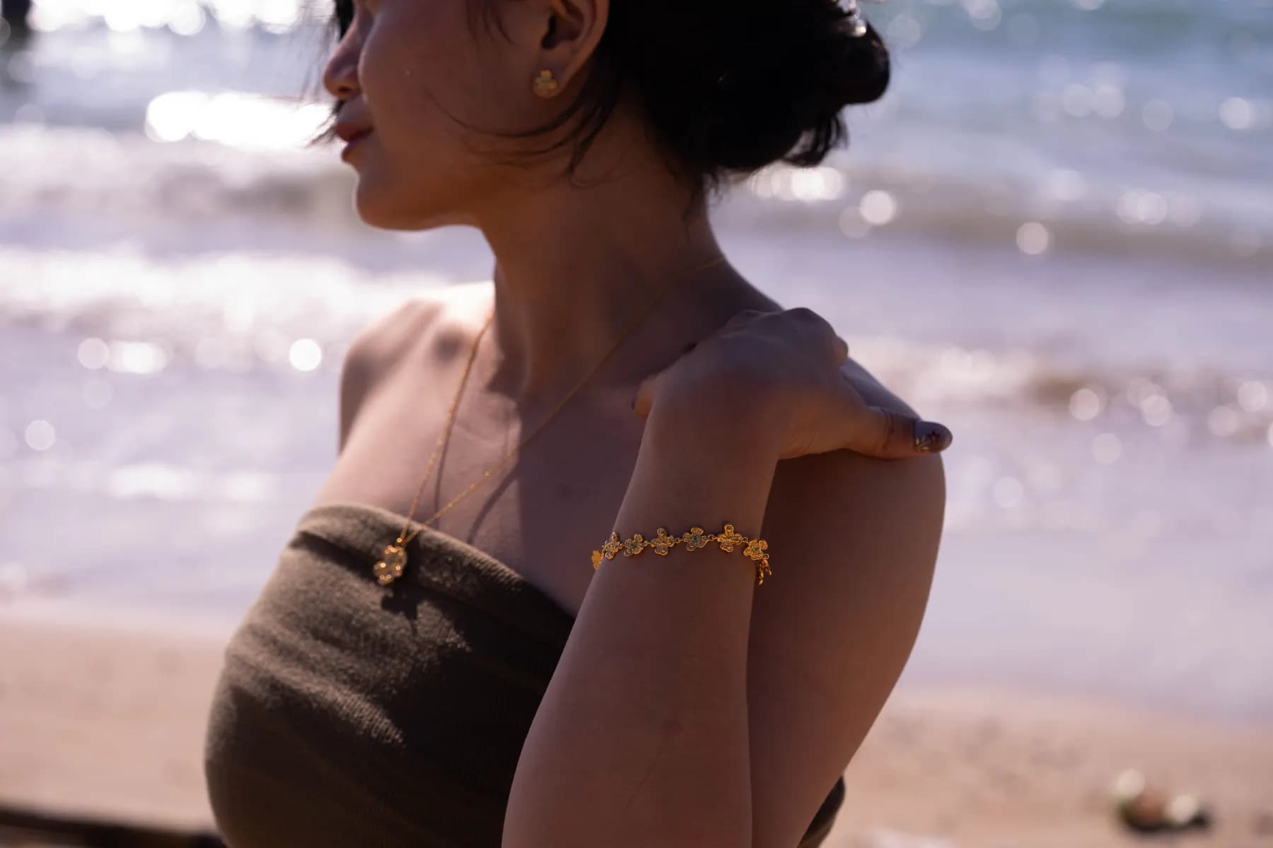 Backlit woman by the sparkling sea wearing a flower pendant and floral bracelet