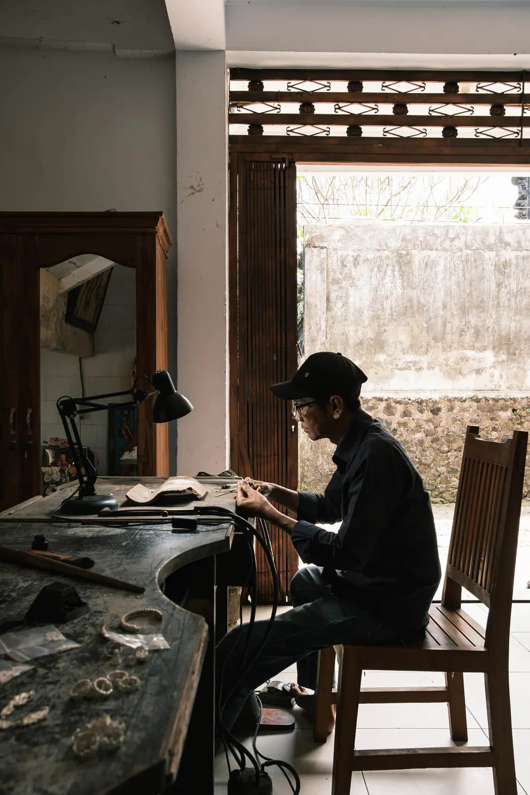 Artisan seated at a curved wooden workbench by an open doorway in the Klungkung studio