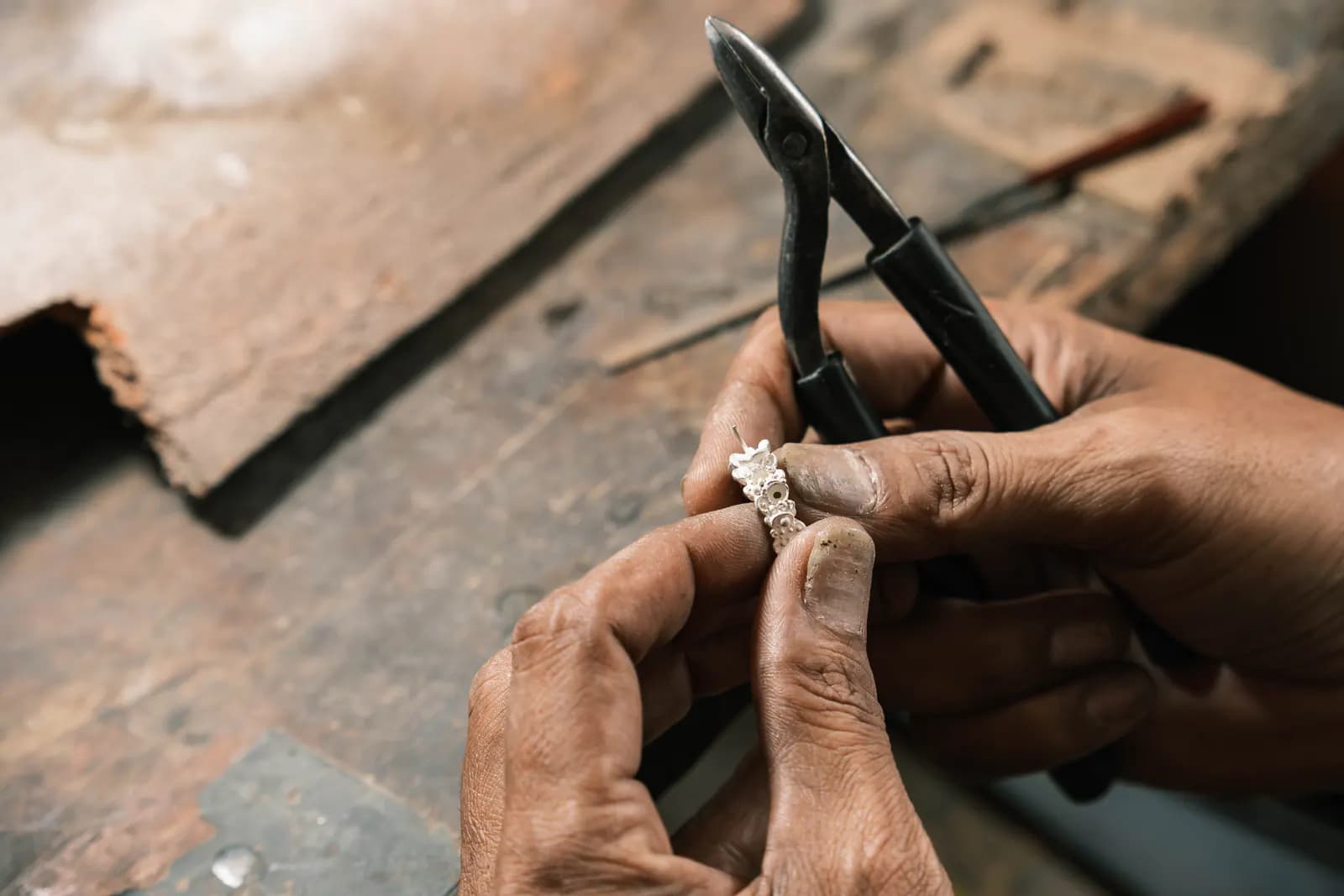 Weathered hands shaping a ring with pliers over a worn bench