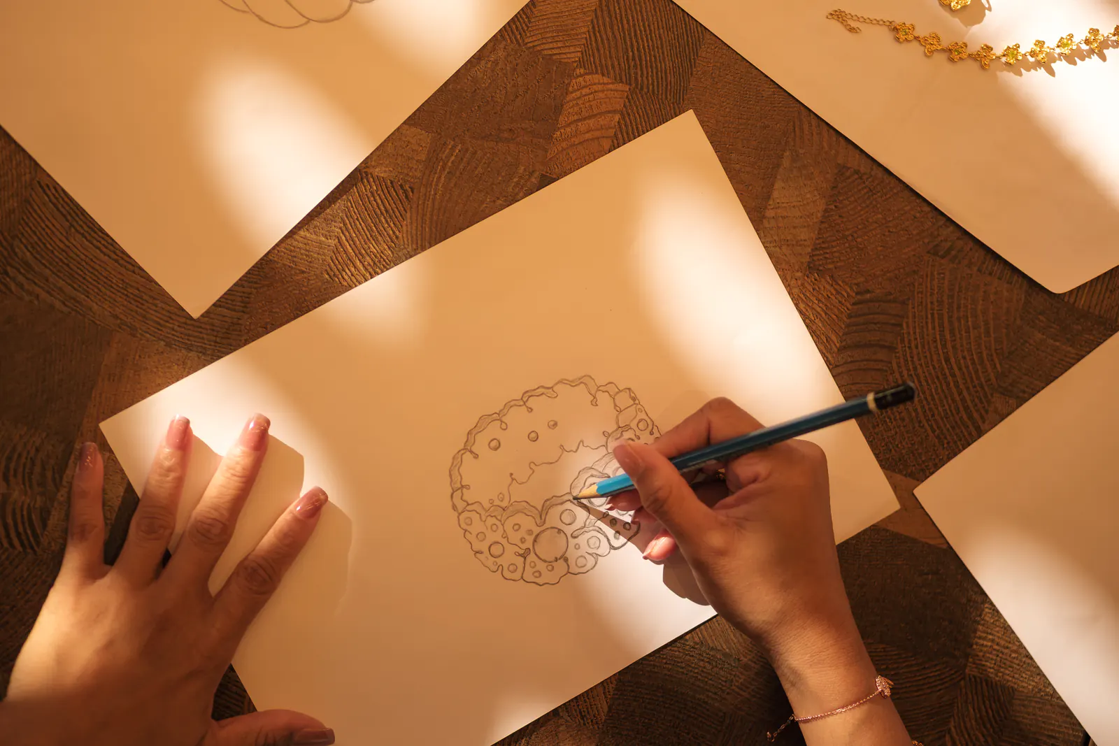 Overhead view of hands sketching a floral jewelry design in pencil